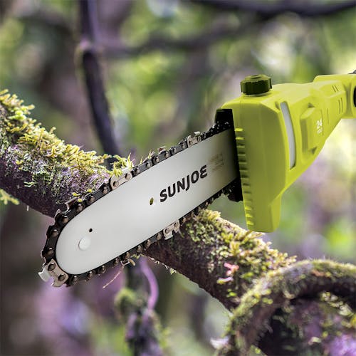 Sun Joe 24-volt cordless telescoping pole 8-inch chainsaw being used to cut a branch off a tree.