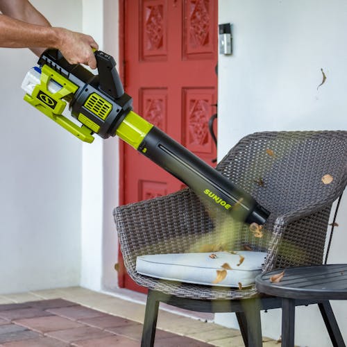 Person using the Sun Joe 48-volt cordless brushless turbine leaf blower to blow leaves off patio furniture.