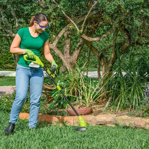 Woman using the Sun Joe 24-Volt cordless and stringless grass trimmer to trim a lawn.