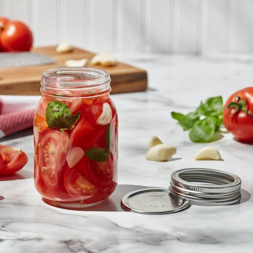 EatNeat 16-ounce Pint Glass Canning Jar filled with sliced tomato with the metal lid next to it on the kitchen counter.