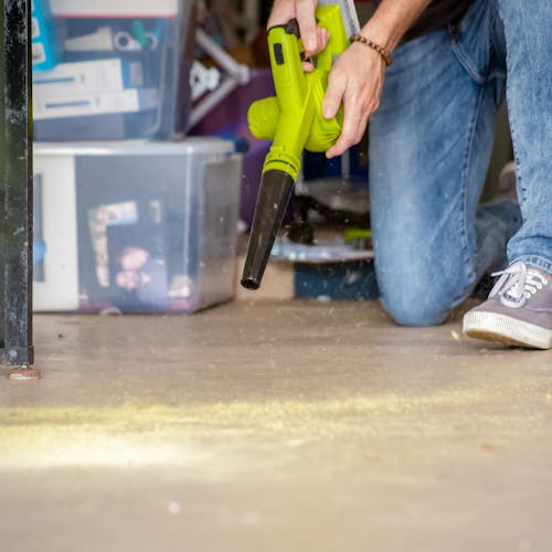 Person using the Sun Joe 24-volt cordless workshop blower with a 2.0-Ah lithium-ion battery attached to blow dust and debris off a floor.