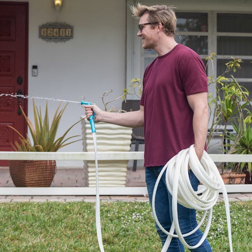 Man using the Aqua Joe 50-foot Fiberjacket RV hose with a hose nozzle to water the grass.