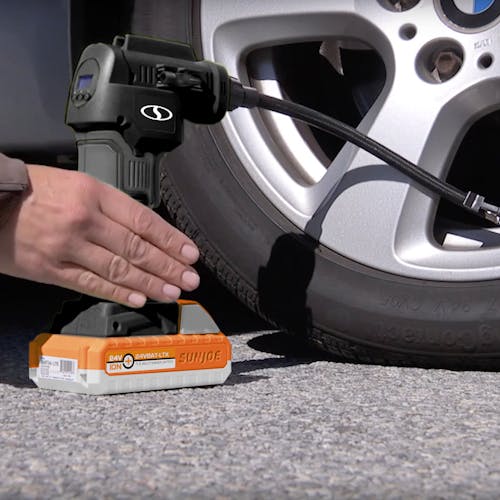 Person using the Sun Joe 24-Volt Cordless Portable Air Compressor in black with a 1.5-Ah lithium-ion Battery attached to fill a car tire.