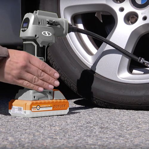 Person using the Sun Joe 24-Volt Cordless Portable Air Compressor in gray with a 1.5-Ah lithium-ion Battery attached to fill a car tire.
