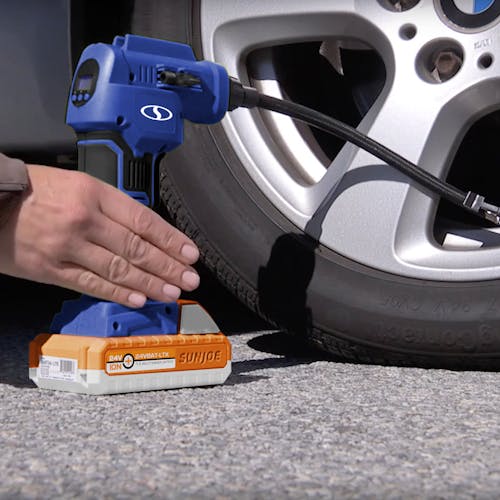 Person using the Sun Joe 24-Volt Cordless Portable Air Compressor in blue with a 1.5-Ah lithium-ion Battery attached to fill a car tire.