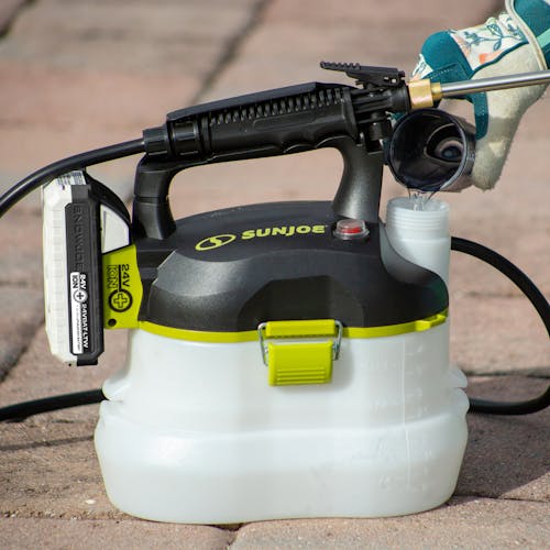 Sun Joe 24-volt cordless Multi-Purpose Chemical Sprayer Kit sitting on paving stones.