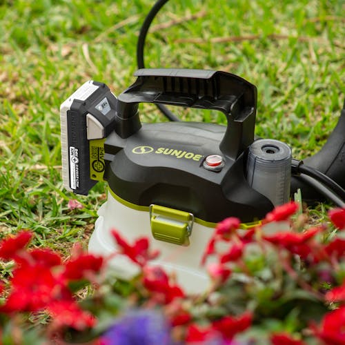 Sun Joe 24-volt cordless Multi-Purpose Chemical Sprayer Kit in the grass with flowers in the foreground.