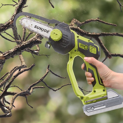 The Sun Joe Cordless Handheld Chainsaw cutting a branch off a tree.