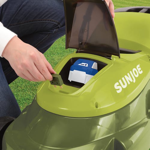 Person opening up the battery compartment of the Sun Joe 24-Volt cordless 14-inch Lawn Mower, showing a 4.0-Ah lithium-ion battery inside.