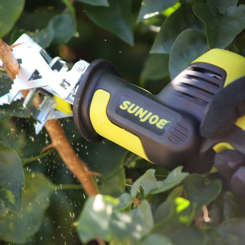 Person using the branch jaw clamp on the Sun Joe 24-volt Cordless All-Purpose Reciprocating Saw Kit to help cut through a branch.