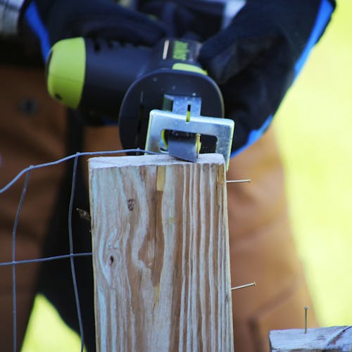 Person using the Sun Joe 24-volt Cordless All-Purpose Reciprocating Saw Kit to cut through a wired fence.