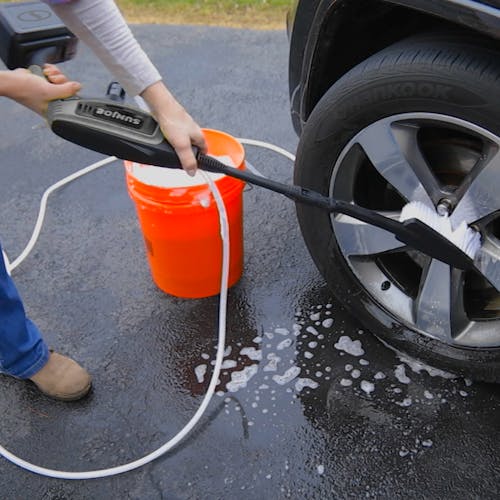 Sun Joe 24-Volt Cordless Power Cleaner in a gray color using the brush attachment to clean the rims of a car.