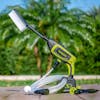 Sun Joe 24-Volt Cordless Power Cleaner outside on the ground with the brush attached and a palm tree in the background.