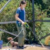 Woman using her Sun Joe 24-Volt Cordless Power Cleaner to clean her patio. Her small dog is behind her.