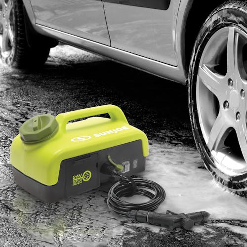 Sun Joe 24-volt cordless portable shower spray washer next to a car with suds in the driveway.