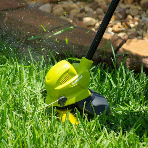Person using the Sun Joe 24-Volt Cordless 10-inch Stringless Grass Trimmer to cut grass.