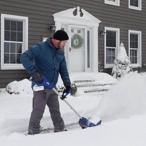 Person using the Snow Joe 24-Volt cordless 11-inch snow shovel kit to clear their walkway.