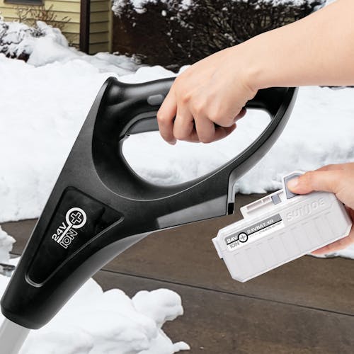 Person attaching a 5.0-Ah lithium-ion battery onto the Snow Joe 24-volt cordless 12-inch snow shovel kit in gray.