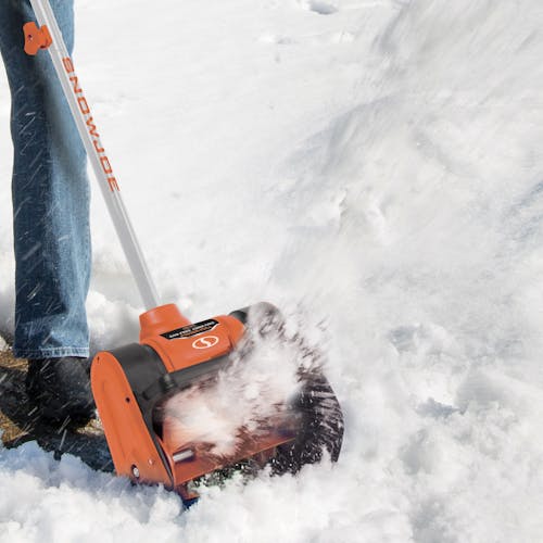 Person using the Snow Joe 24-volt cordless 12-inch snow shovel kit in orange to clear snow.