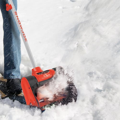 Person using the Snow Joe 24-volt cordless 12-inch snow shovel kit in red to clear snow.