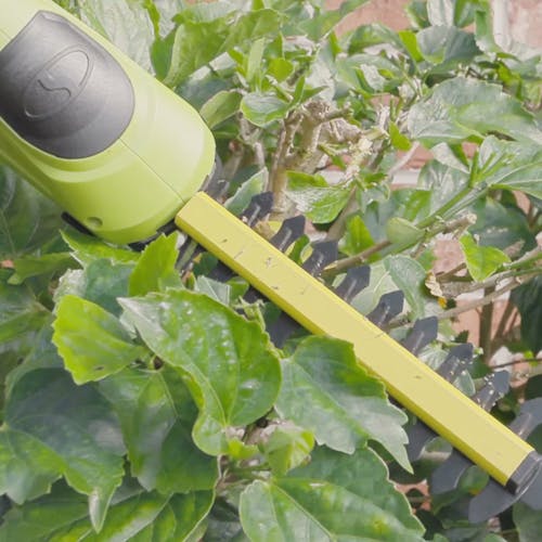 Person using the Sun Joe 24-volt Cordless handheld shrubber and trimmer to trim a bush.