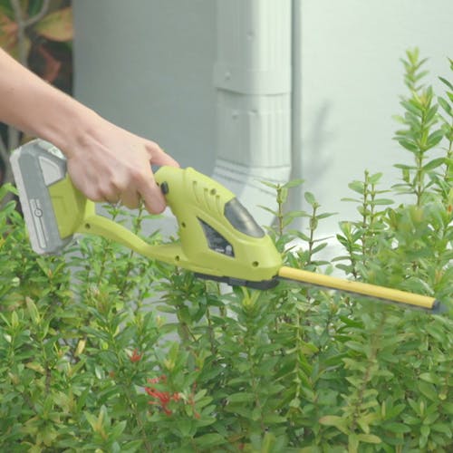 Person using the Sun Joe 24-volt Cordless handheld shrubber and trimmer to trim plants.