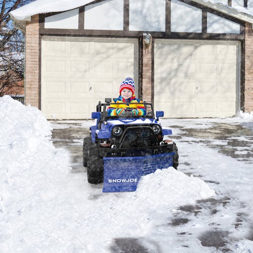 Child using toy plow to clear small amount of snow from driveway