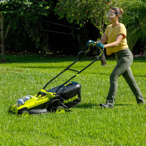 Woman using the Sun Joe 48-volt cordless 17-inch lawn mower kit to mow a lawn.