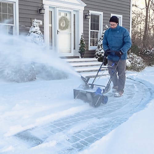 Man using the Snow Joe 48-volt cordless 18-inch snow blower kit to clear a front walkway of snow.