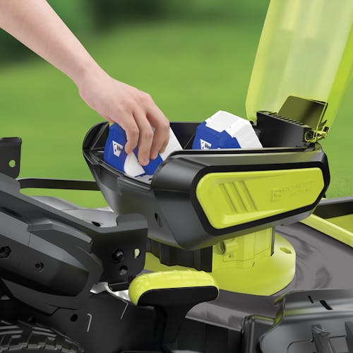Close-up of the battery compartment on the Sun Joe 48-volt cordless self-propelled 21-inch lawn mower with someone inserting two 4.0-Ah lithium-ion batteries.