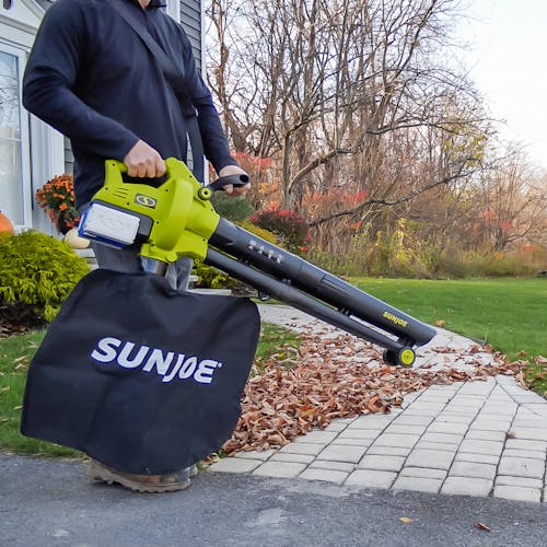 Person using the Sun Joe 48-volt cordless leaf blower, vacuum, mulcher with wheels to blow leaves off a walkway.