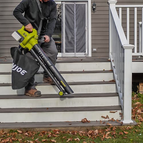 Person using the Sun Joe 48-volt cordless leaf blower, vacuum, mulcher with wheels to blow leaves off the steps of a patio.