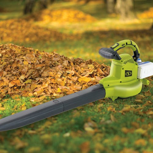 Sun Joe 48-volt cordless leaf blower, vacuum, mulcher kit with two 4.0-Ah lithium-ion batteries attached laying in grass next to a pile of leaves.