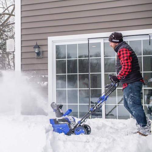 Person using the Snow Joe 48-volt cordless snow blower kit with auto-rotate chute to clear a patio deck of snow.
