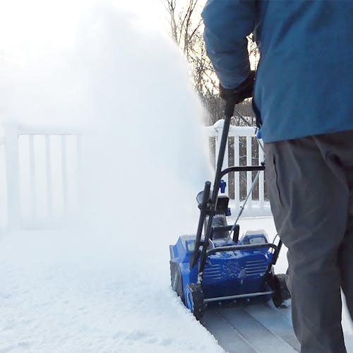 Person using the Snow Joe 48-volt cordless 18-inch snow blower kit to clear a patio deck of snow.
