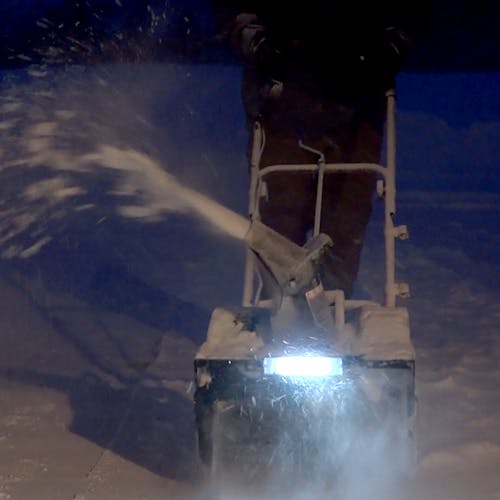 Person using the Snow Joe 48-volt cordless 18-inch snow blower kit at night with the LED light on to clear a path of snow.