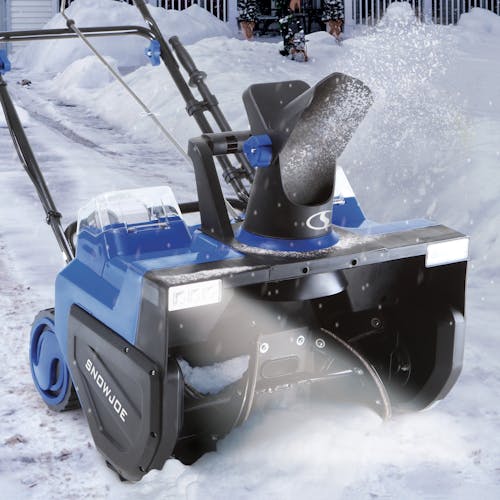 Snow Joe 48-volt cordless 22-inch single-stage snow blower kit outside in the snow with the LED headlights on.