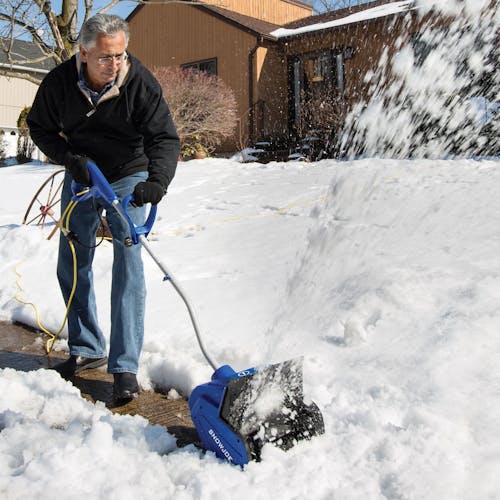 Man using the Snow Joe 10-amp 13-inch electric snow shovel to throw snow off a sidewalk.