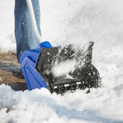 Close-up of the Snow Joe 10-amp 13-inch electric snow shovel blowing snow off a sidewalk.
