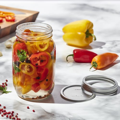 EatNeat 32-ounce quart wide mouth glass canning jar filled with sliced peppers with the metal lid next to it on the kitchen counter.
