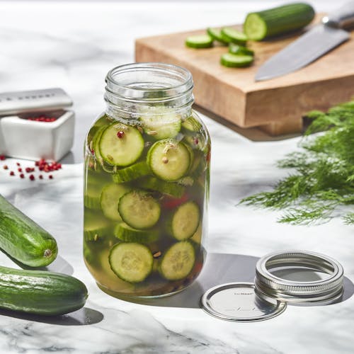EatNeat 32-ounce Quart Glass Canning Jar filled with sliced pickles with the metal lid next to it on a kitchen counter.