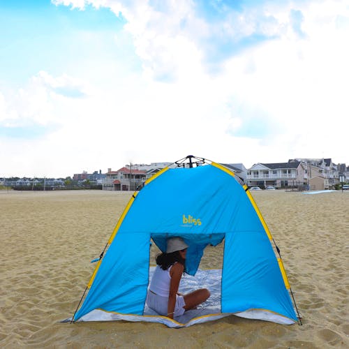 Rear view of the pop-up beach tent on the sand with a woman looking out from the opened back window flap.