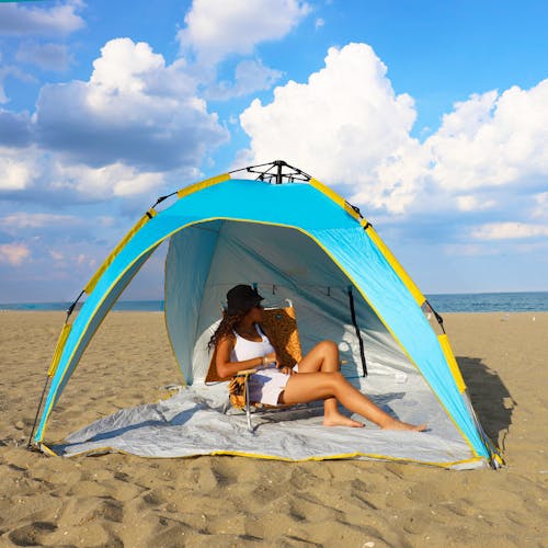 Woman relaxing in a chair on the beach while being shaded by the pop-up beach tent.