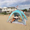 Man relaxing in a chair on the beach while being shaded by the pop-up beach tent.