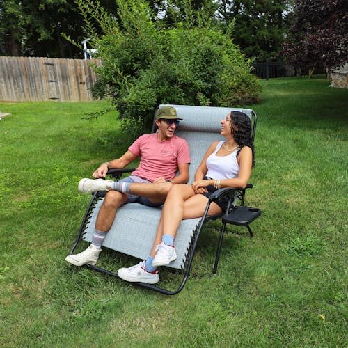 Couple sitting together on the 45-inch 2-Person Geometric Grey Gravity Free Recliner on a lawn.