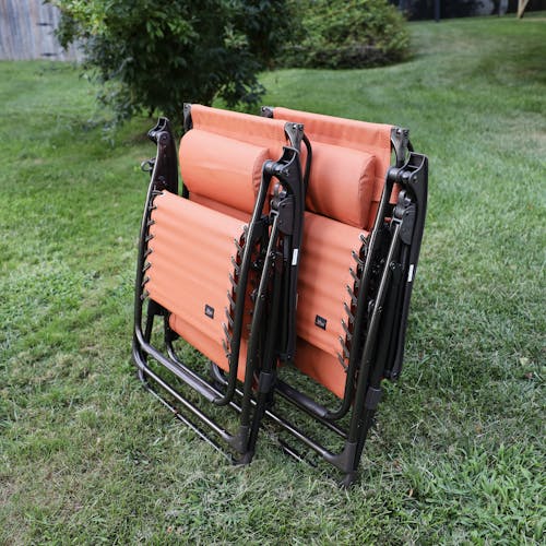 Angled view of a set of 2 26-inch terracotta gravity free chairs folded on a lawn.