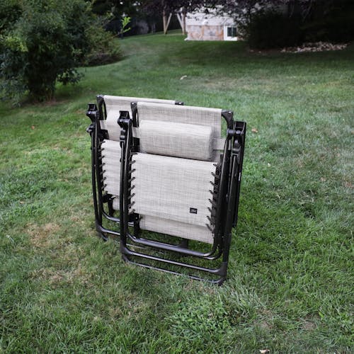Set of 2 26-inch sand gravity free chairs folded and standing on a lawn.