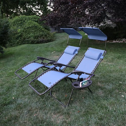 Angled view of a Set of 26-inch denim blue gravity free chairs reclined on a lawn.