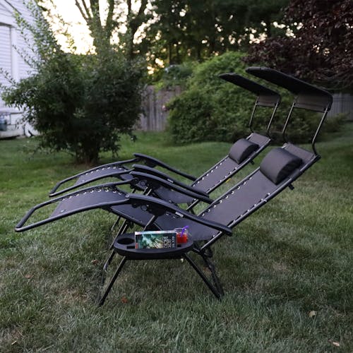 Side view of a set of 2 26-inch black gravity free chairs reclined on a lawn.