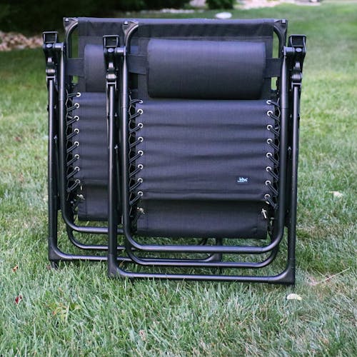 Set of 2 26-inch black gravity free chairs folded and standing on a lawn.